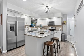 A modern kitchen with stainless steel appliances, a marble island, and a view to the outside. - The Birch: Poconos Getaway • Hot Tub, Game Room, Fire Pit • Sleeps 10 (Blakeslee)