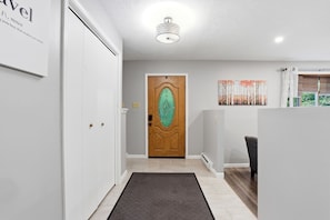 A hallway with a wooden door, a reception desk, and a painting on the wall. - The Birch: Poconos Getaway • Hot Tub, Game Room, Fire Pit • Sleeps 10 (Blakeslee)