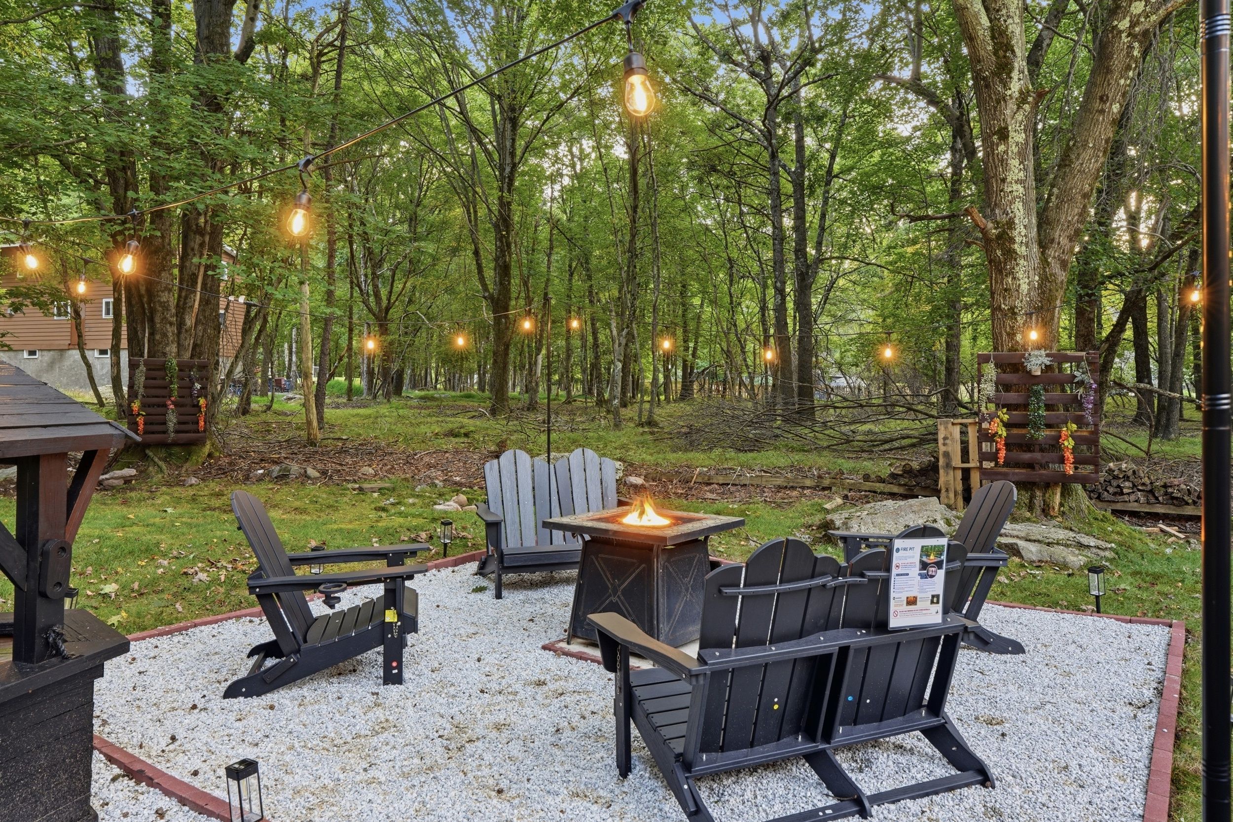 An outdoor seating area with Adirondack chairs, a fire pit, and string lights.