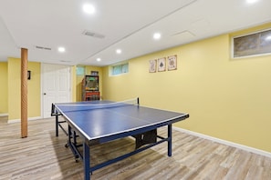 A room with a ping pong table, a door, a window, and a wall-mounted game machine. - The Birch: Poconos Getaway • Hot Tub, Game Room, Fire Pit • Sleeps 10 (Blakeslee)