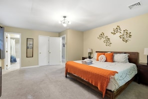 Quarto com cama, mesa de cabeceira, abajur, planta na parede e uma porta.
