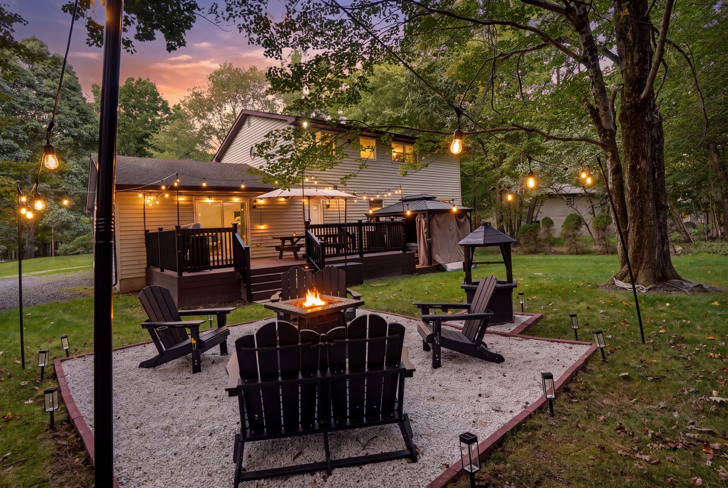 An outdoor patio area with Adirondack chairs, a fire pit, and string lights.