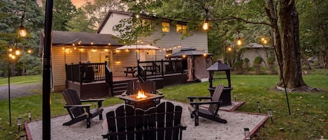 An outdoor patio area with Adirondack chairs, a fire pit, and string lights.