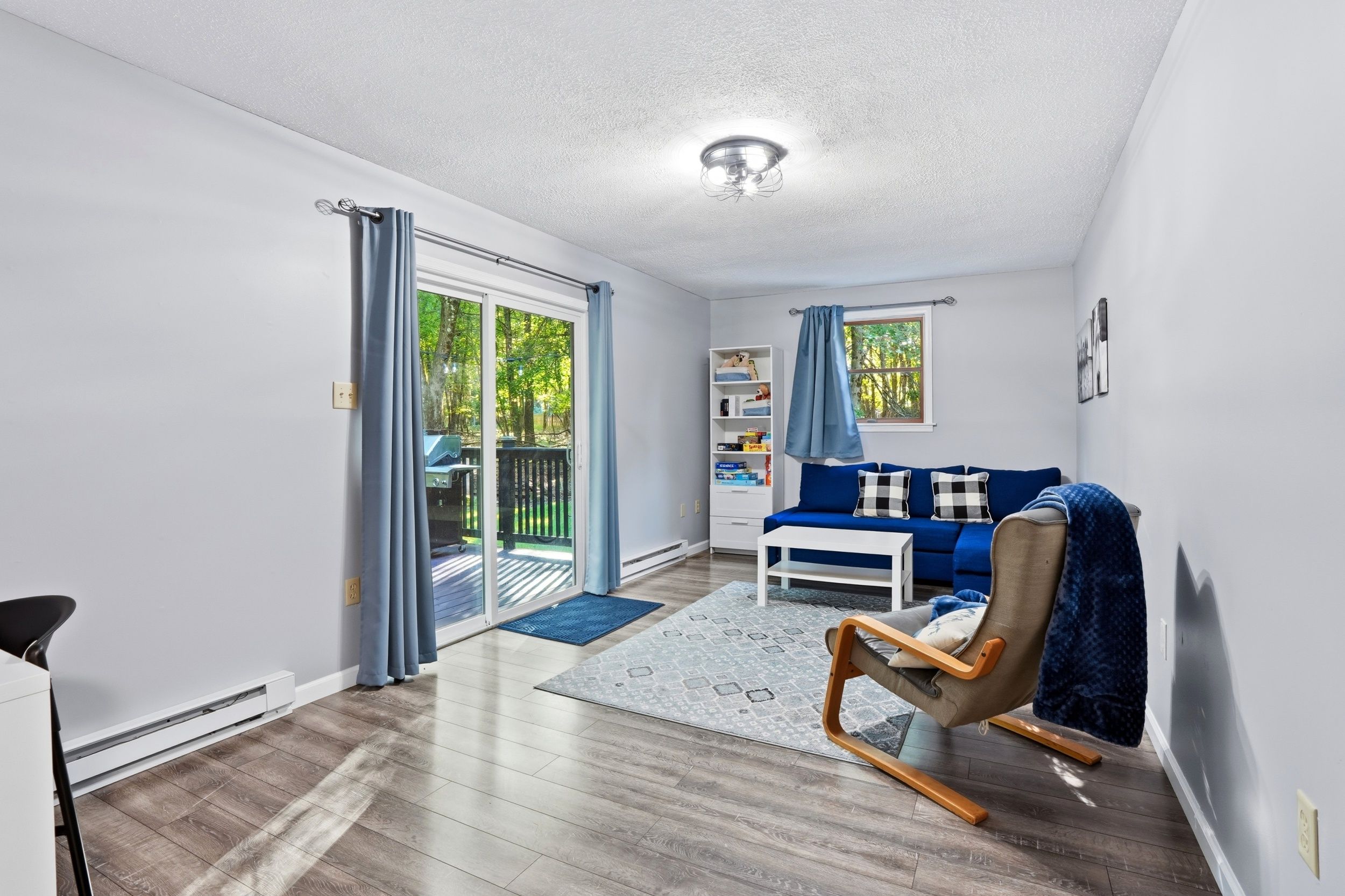 Ein modernes Wohnzimmer mit einer Schiebeglastür, die auf einen Balkon führt, einem blauen Sofa, einem Holzschaukelstuhl und einem weißen Couchtisch.