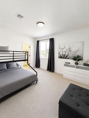 Een moderne slaapkamer met een stapelbed, een bureau met lades, een potplant en een schilderij aan de muur.