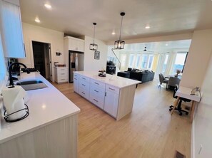 A modern kitchen with white cabinetry, a central island, and a dining area with a black sofa. - Gorgeous 3-bedroom condo in charming Cedar City perfect for relaxing (Cedar City)