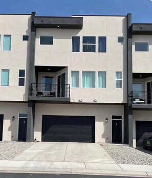 A modern multi-story residential building with a flat roof, large windows, and a covered outdoor seating area.