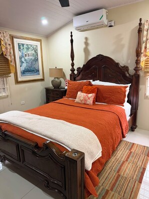 A neatly made bed with a wooden headboard, a bedside lamp, and a framed picture on the wall. - Charming 3-bedroom 2BTH house in Drax Hall with solar WiFi beach access pool (St. Ann Parish)
