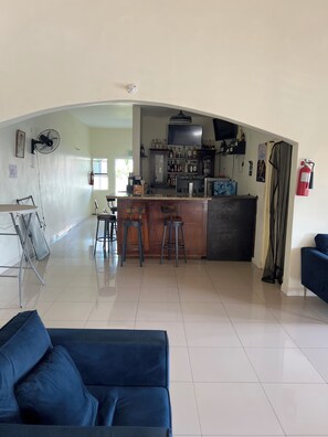 A spacious living area with a dark blue sofa, a kitchen with a bar area, and a fire extinguisher mounted on the wall. - Charming 3-bedroom 2BTH house in Drax Hall with solar WiFi beach access pool (St. Ann Parish)