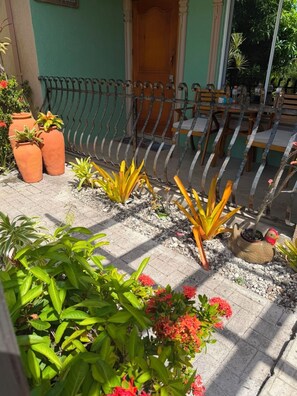 A patio with a metal fence, potted plants, and a chicken-shaped planter. - Charming 3-bedroom 2BTH house in Drax Hall with solar WiFi beach access pool (St. Ann Parish)