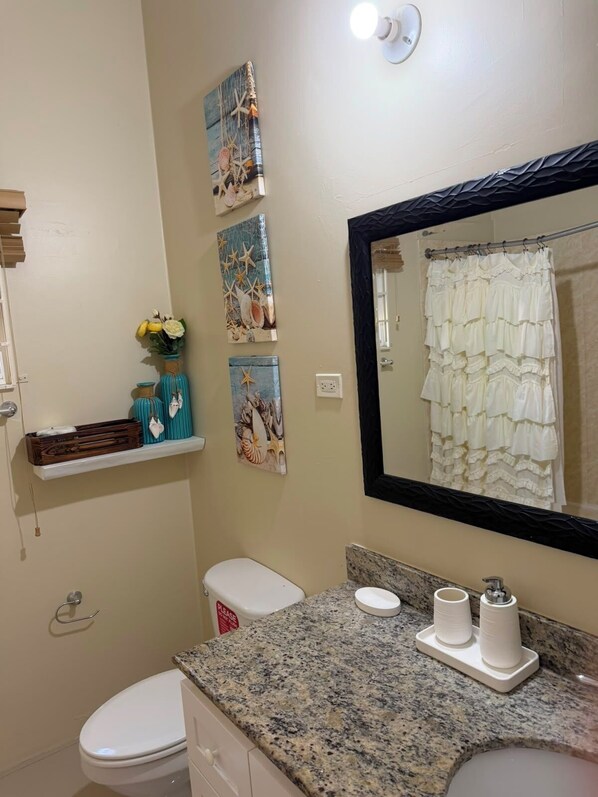 A bathroom with a toilet, sink, and mirror. There are decorative items on the wall and a towel rack. - Charming 3-bedroom 2BTH house in Drax Hall with solar WiFi beach access pool (St. Ann Parish)