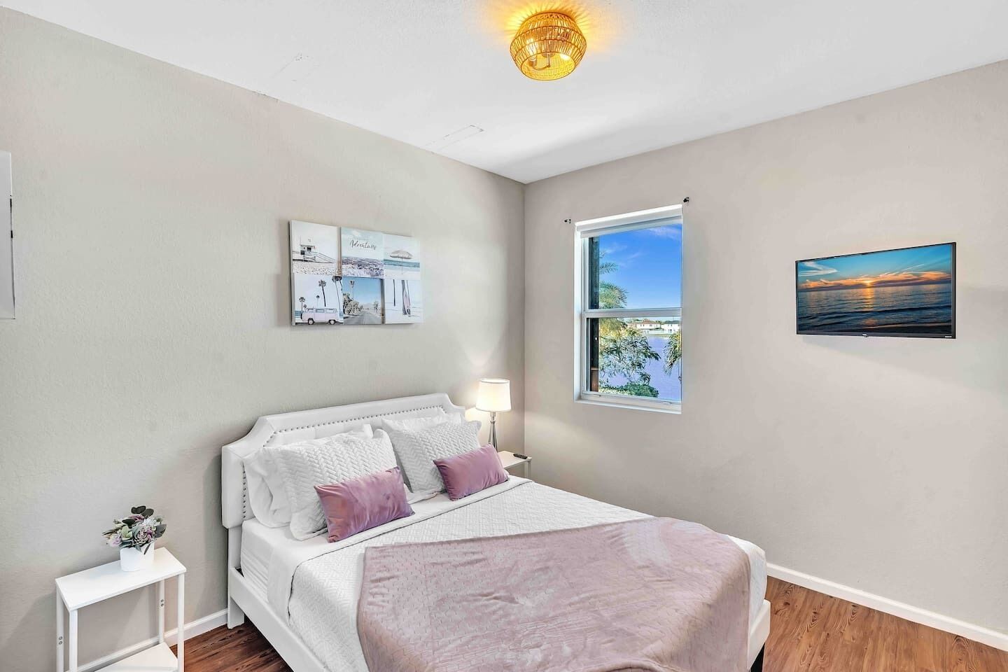 Une chambre à coucher comprenant un lit, une table de chevet, une lampe, une fenêtre avec vue et des œuvres d’art murales.