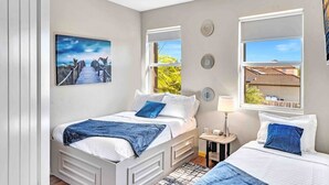 Un dormitorio con dos camas, una mesita de noche, una lámpara y un cuadro de una playa.