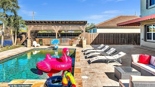 Un patio trasero con piscina, sillas de descanso, zona de barbacoa y un flotador con forma de flamenco.