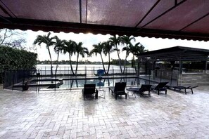 An outdoor seating area with a view of the sea, palm trees, and a covered structure.