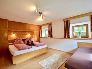Ein Schlafzimmer mit einem hölzernen Bett, einem Nachttisch, einer Fensterbank, Vorhängen und einer Deckenleuchte.