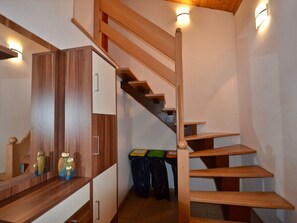 Eine Holzt Treppe mit Handlauf, eine Zwischenebene mit Schrank und ein Mülleimer mit farbigen Etiketten.