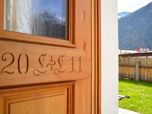 Eine Holztür mit eingekerbten Zahlen '20' und '11' sowie ein Blick auf eine Berglandschaft durch ein Fenster.