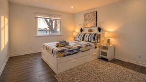 Un dormitorio con cama, mesitas de noche, una ventana y un cuadro en la pared.