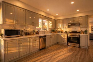 A modern kitchen with stainless steel appliances, wooden cabinets, and a large window providing natural light. - Grand Villa in Scarborough Family Escape (Toronto)