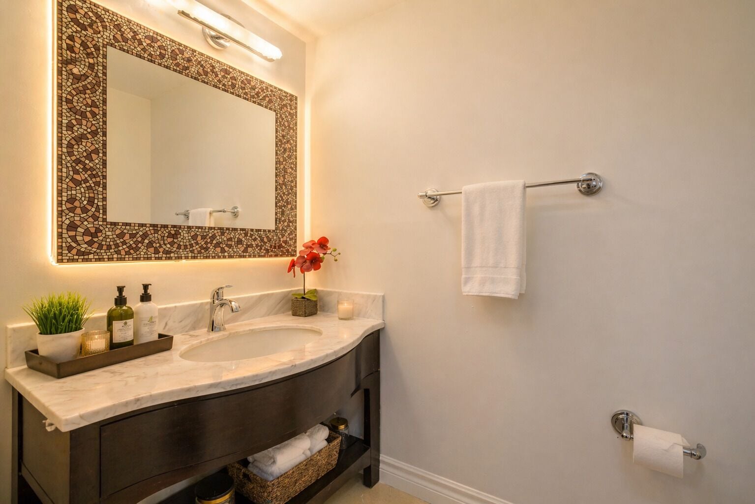 A bathroom with a large mirror, a sink, a towel rack, and a toilet paper holder.