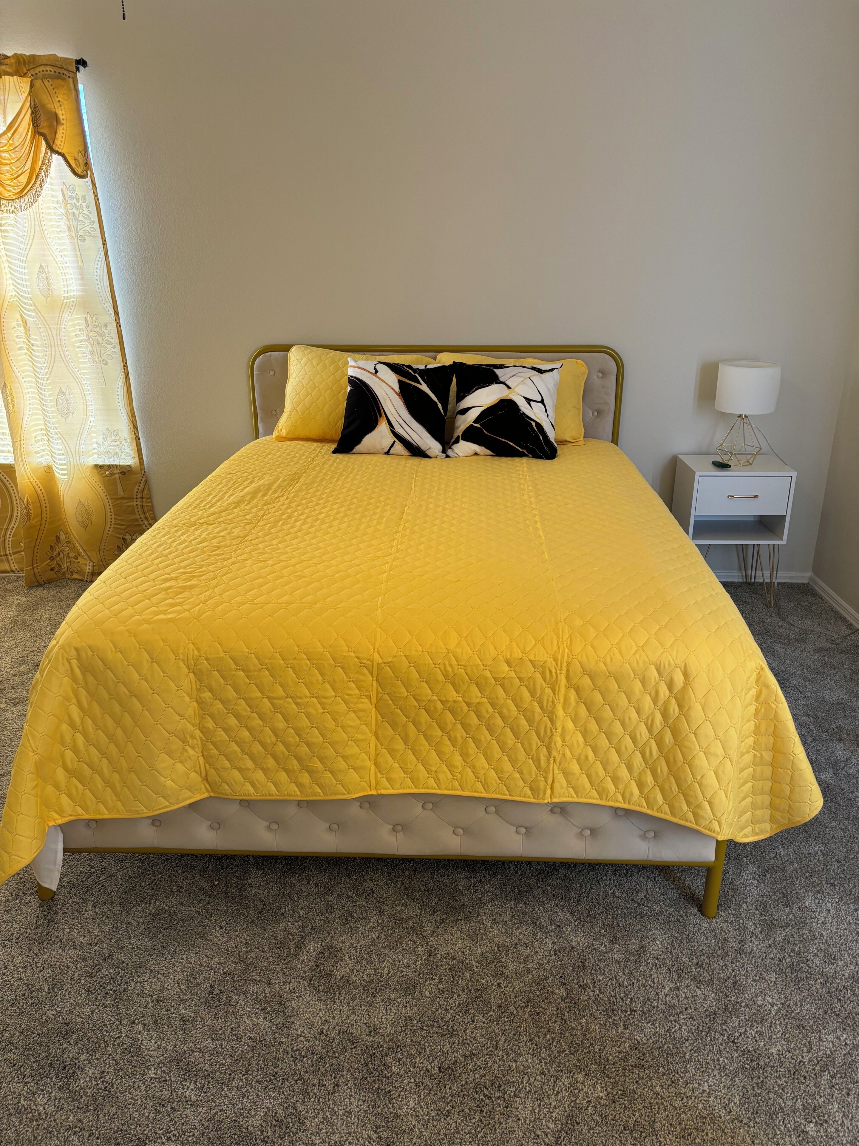 Un lit recouvert d’une courtepointe jaune, avec une tête de lit et deux oreillers à motifs noir et blanc.