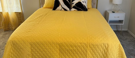 Un lit recouvert d’une courtepointe jaune, avec une tête de lit et deux oreillers à motifs noir et blanc.