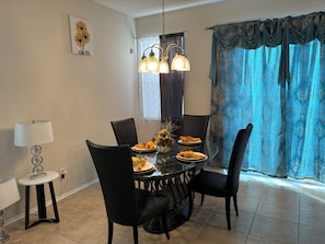 A dining area with a round glass table, black chairs, a chandelier, and a window with patterned curtains. - Enjoyable 4-bedroom townhome with AC in charming Sanford (Sanford)
