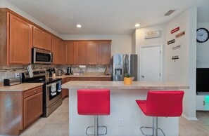 A kitchen with wooden cabinets, stainless steel appliances, a central island with red bar stools, and a wall clock. - Enjoyable 4-bedroom townhome with AC in charming Sanford (Sanford)
