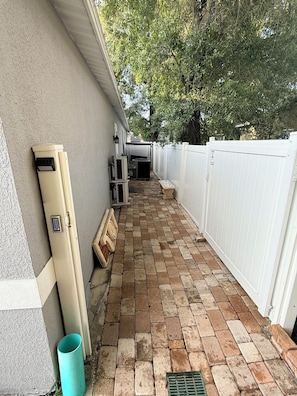A narrow outdoor corridor with a brick floor, a white fence, and a beige wall.