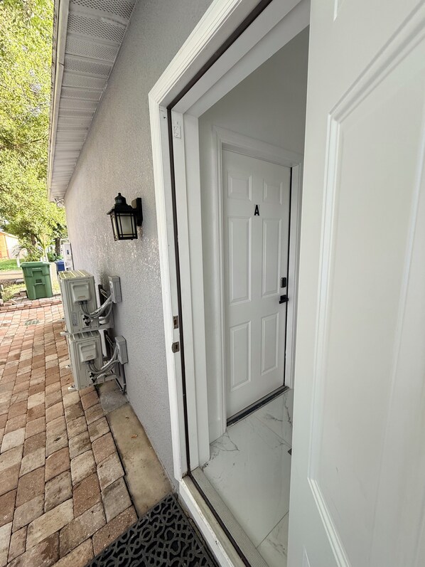 A white door with a number 'A' on it, a wall-mounted light fixture, and electrical boxes on the exterior wall.