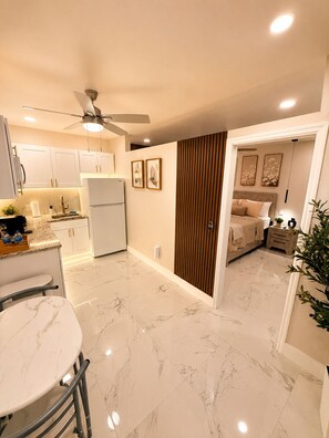 A modern kitchen with white cabinets, a marble countertop, and a ceiling fan.
