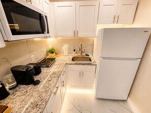A modern kitchen with white cabinets, a stainless steel sink, a built-in microwave, and a white refrigerator.