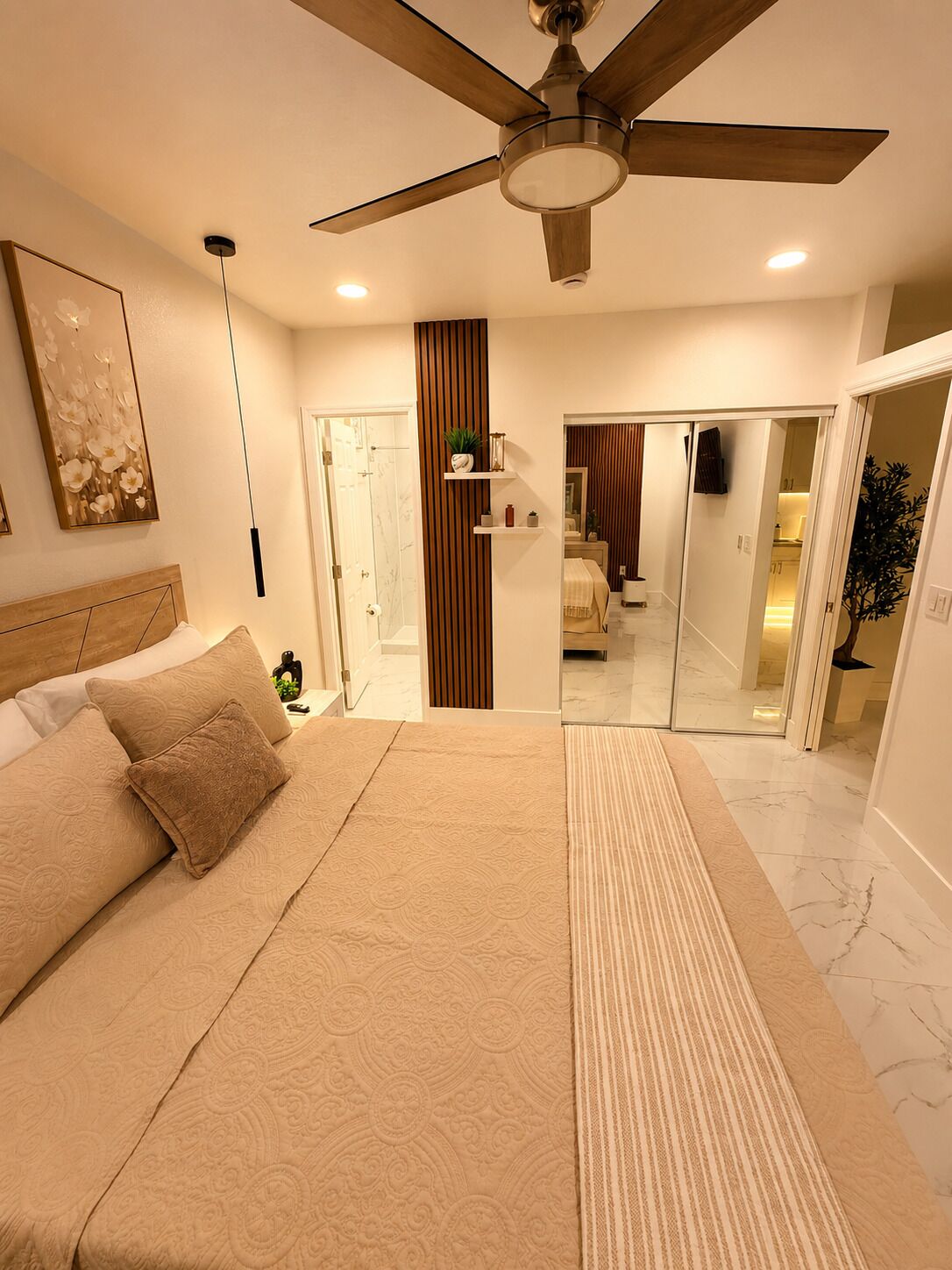 A bedroom with a bed, a ceiling fan, a bedside table, a mirror, and a sliding door leading to a bathroom.