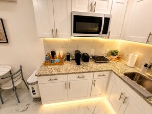 A modern kitchen with white cabinets, a built-in microwave, a granite countertop, and a stainless steel sink.