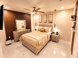 Ein Schlafzimmer mit Bett, Deckenventilator, Nachttisch, Kommode, Spiegel und Wandbildern.
