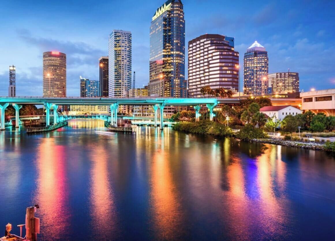 A city skyline with modern high-rise buildings, a bridge over a river, and a calm water body reflecting the lights.