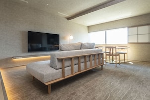 A modern living room with a sofa, a flat-screen TV, a table, and chairs.