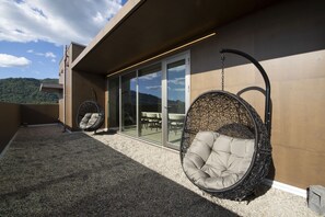 A modern outdoor seating area with two hanging chairs and a glass door leading to an indoor space.