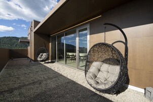 Un área de estar exterior moderna con dos sillones colgantes y un ventanal de vidrio que da a un espacio interior.