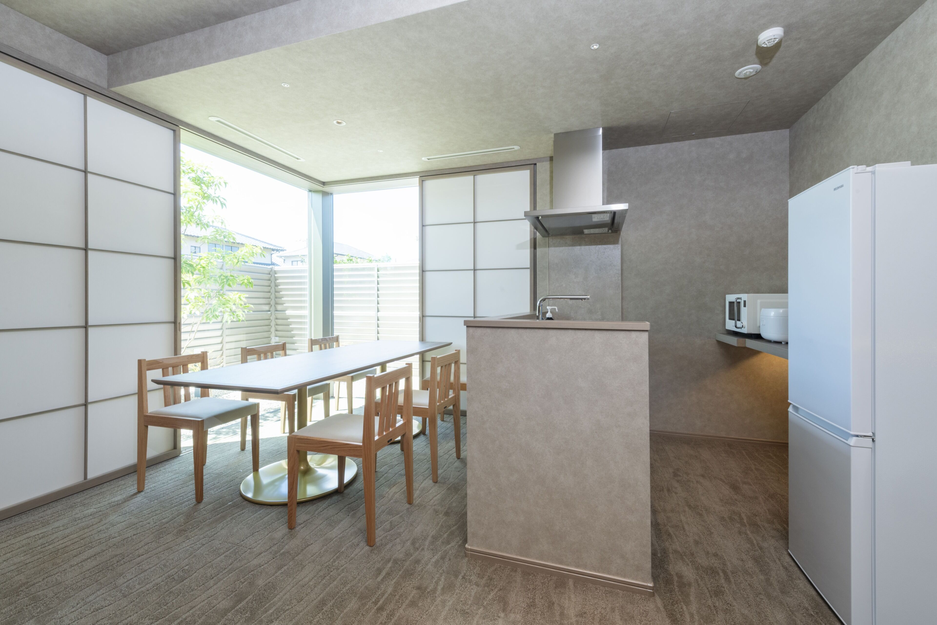 Uma cozinha moderna com área de refeições, apresentando uma ilha central, cadeiras de madeira e uma geladeira branca.