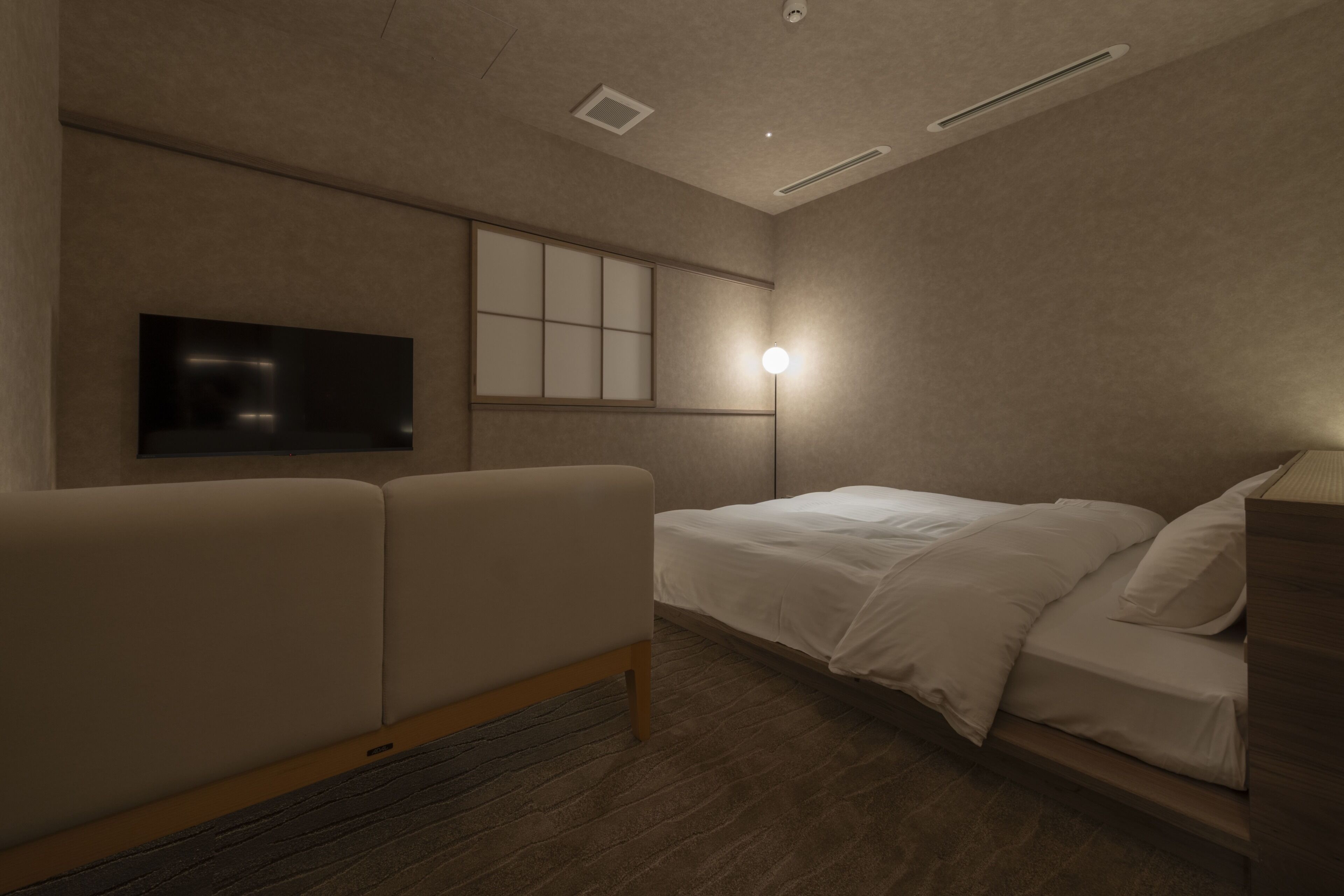 A hotel room with a bed, a sofa, a flat-screen TV mounted on the wall, and a bedside table.