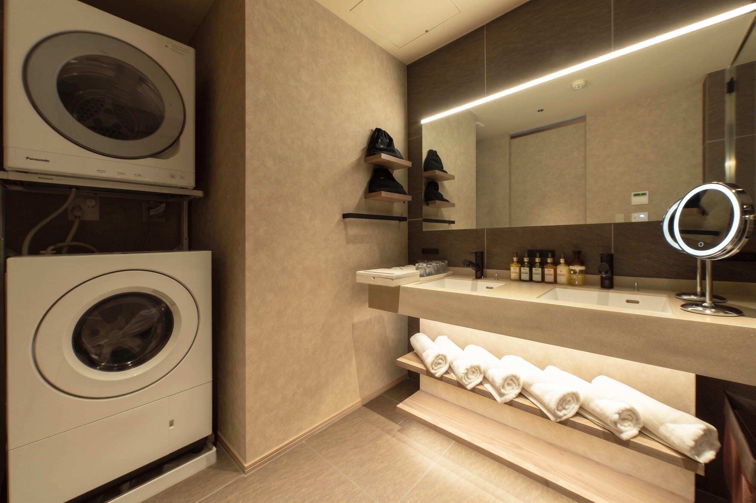 A modern bathroom with a built-in washing machine, a vanity with a mirror, and shelves for towels and toiletries.
