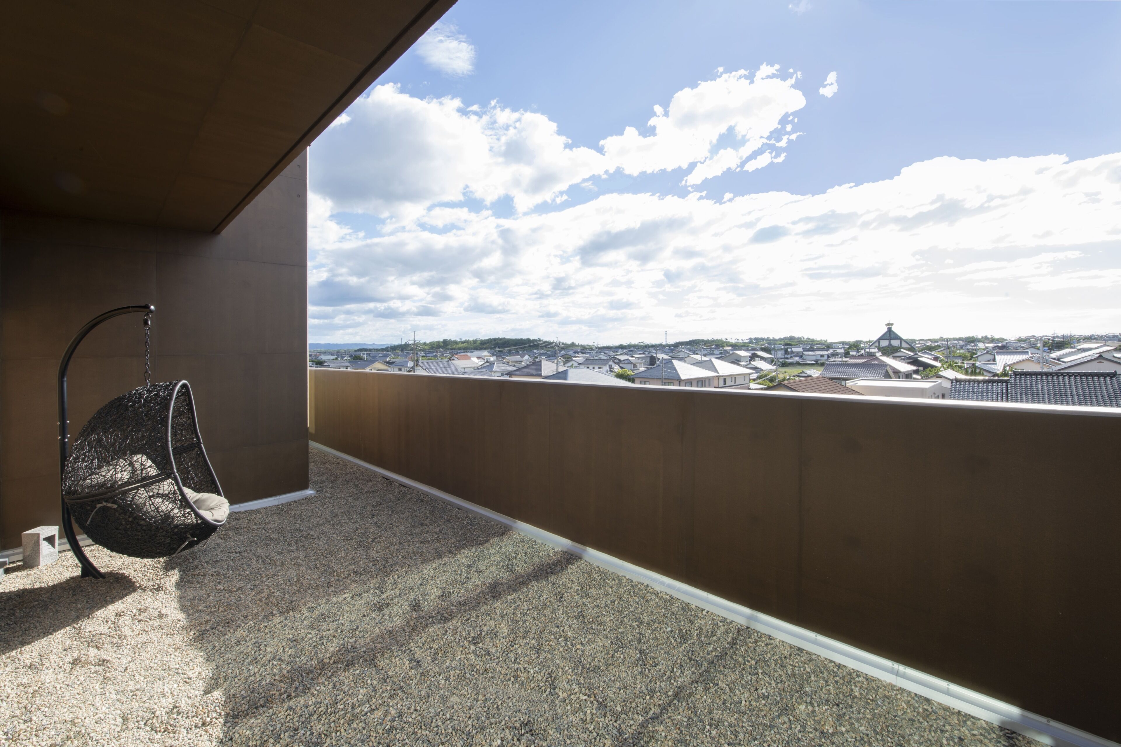 A balcony with a hanging chair, a view of a town with traditional buildings, and a clear sky.