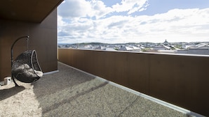 Un balcón con una silla colgante, vista a un pueblo con edificios tradicionales y cielo despejado.