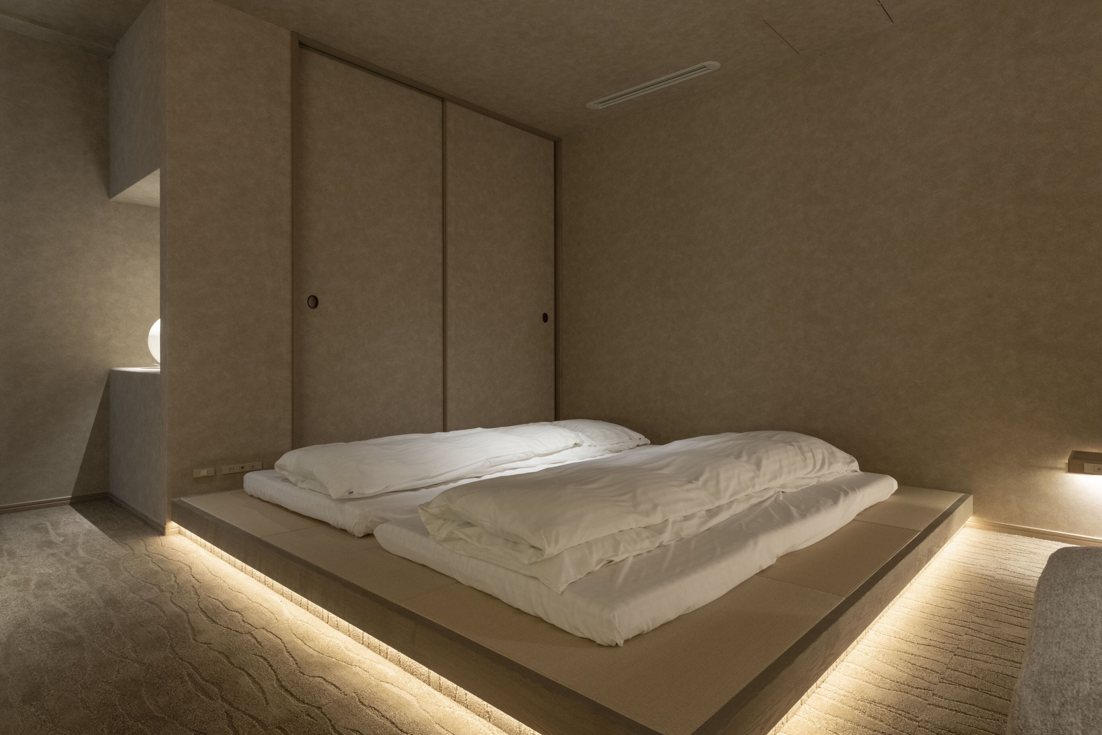 A minimalist bedroom with a single bed, a wardrobe, and a light fixture.