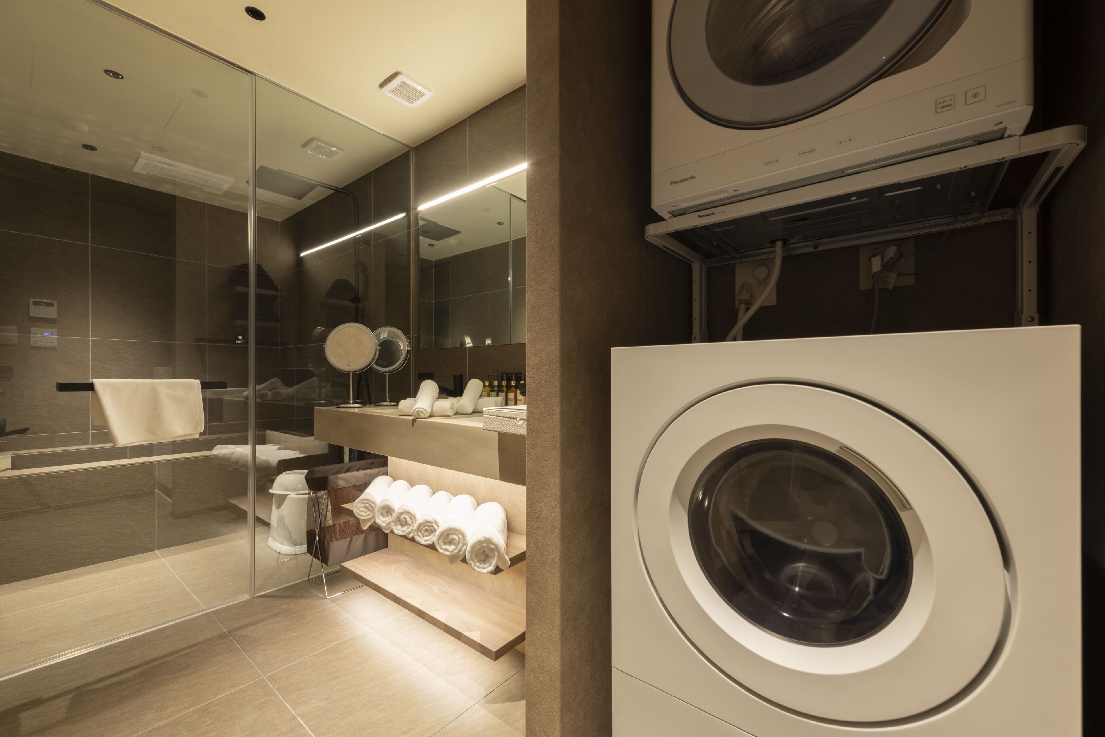 A modern bathroom with a glass shower enclosure, a built-in washing machine, and a vanity with a mirror.