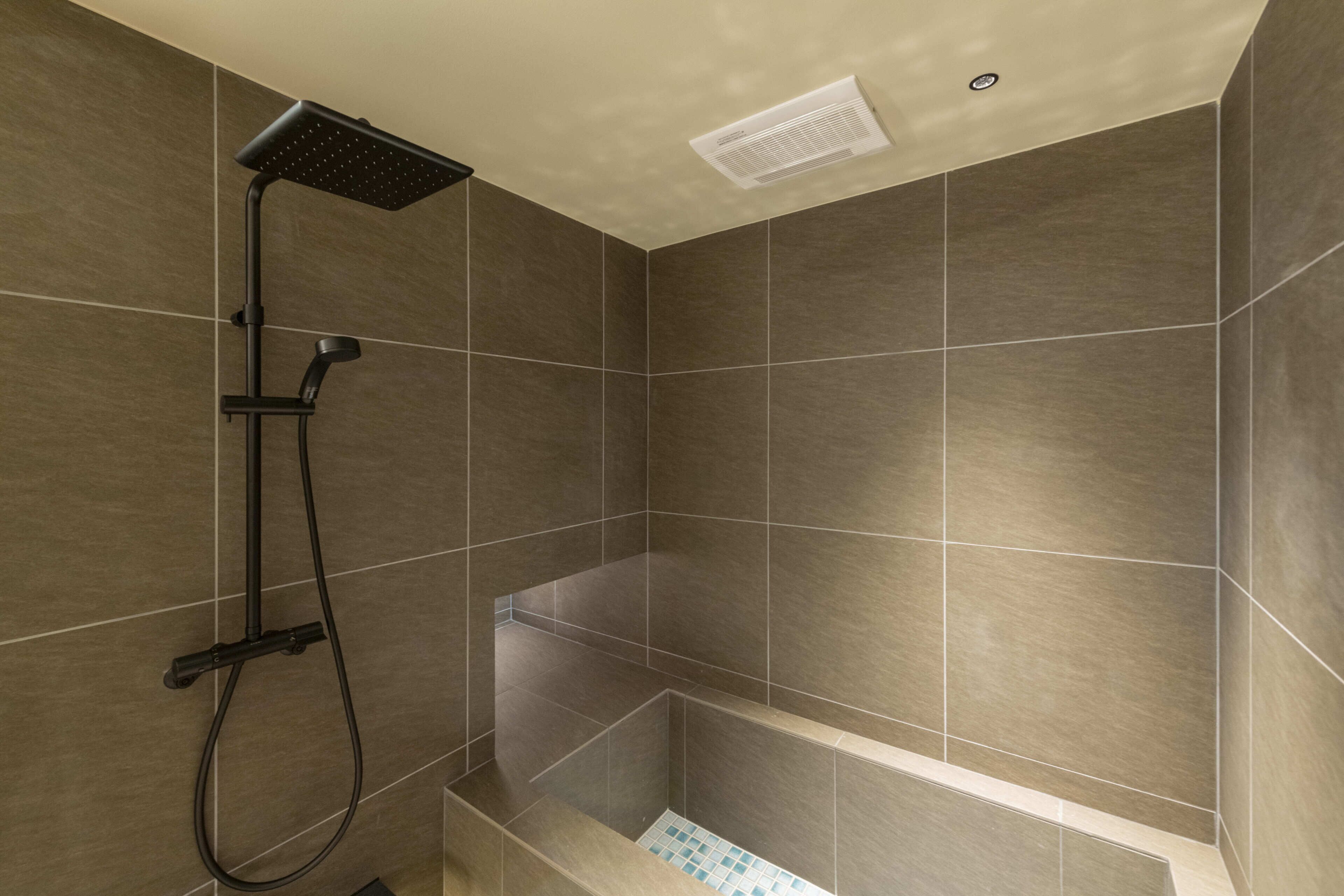 A shower area with a handheld showerhead and a wall-mounted control panel.