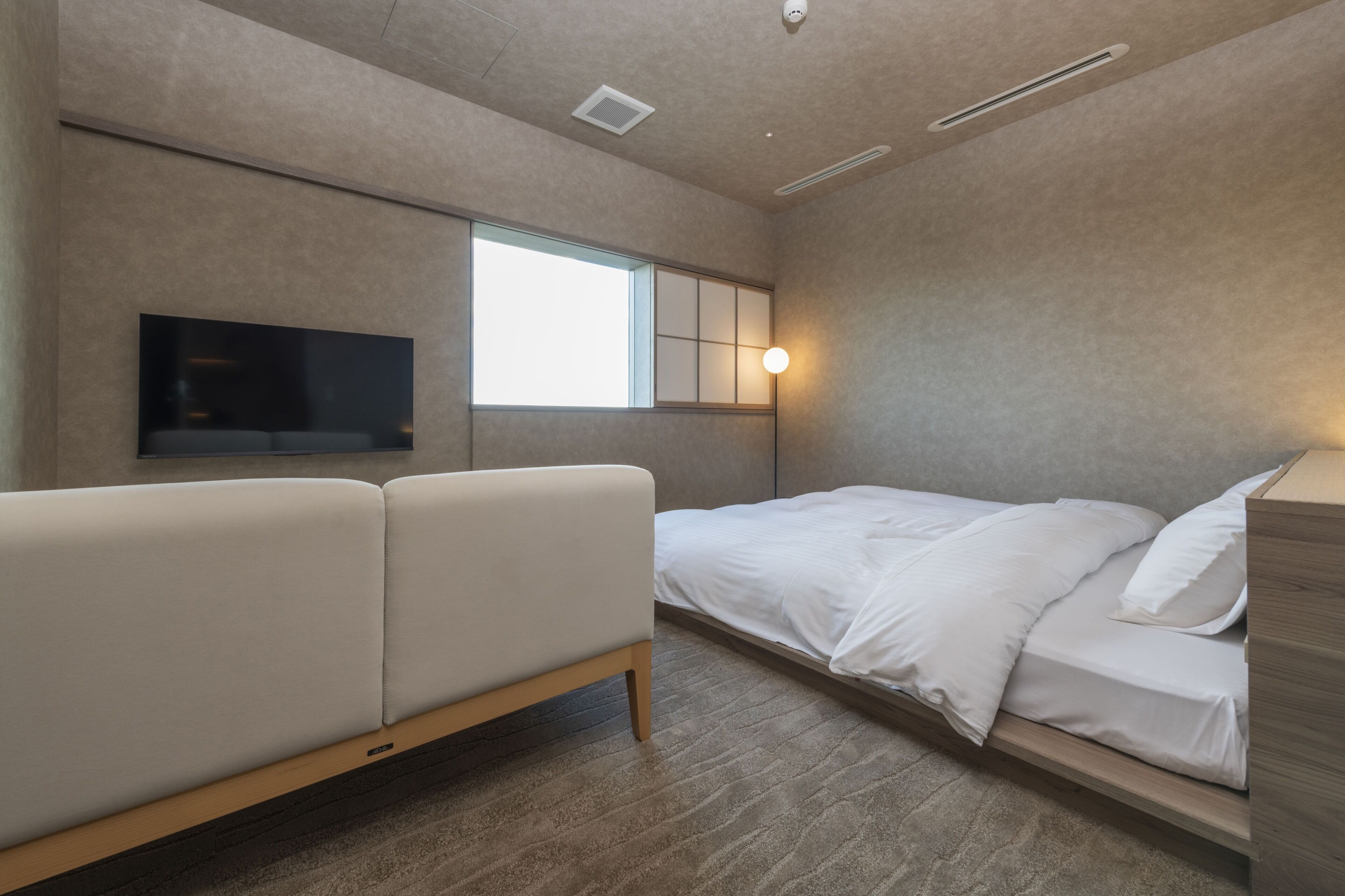 Um quarto moderno com cama, sofá, televisão e janela.