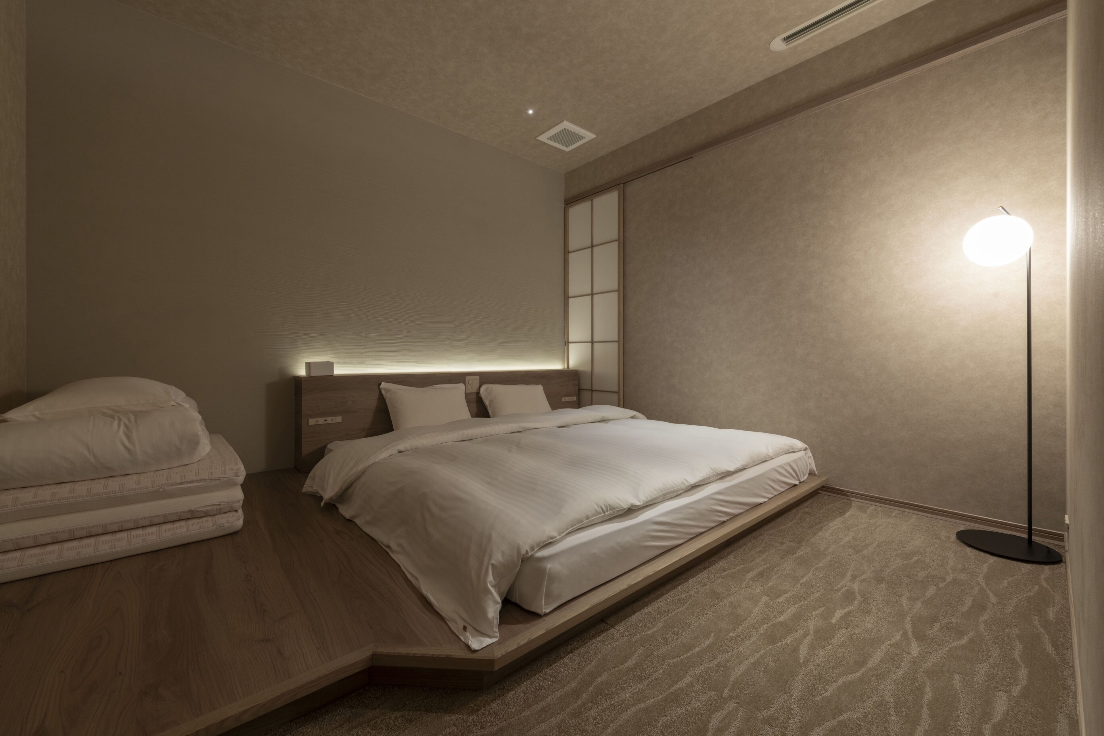 Une chambre moderne avec un lit, des tables de chevet, une lampe sur pied et une étagère intégrée.